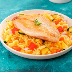 Filete de tilapia dorado servido sobre pasta orzo con vegetales