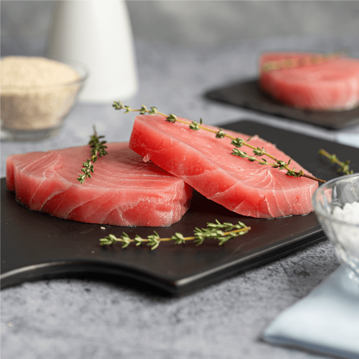 Steak de atún crudo, corte grueso, sobre tabla con romero fresco
